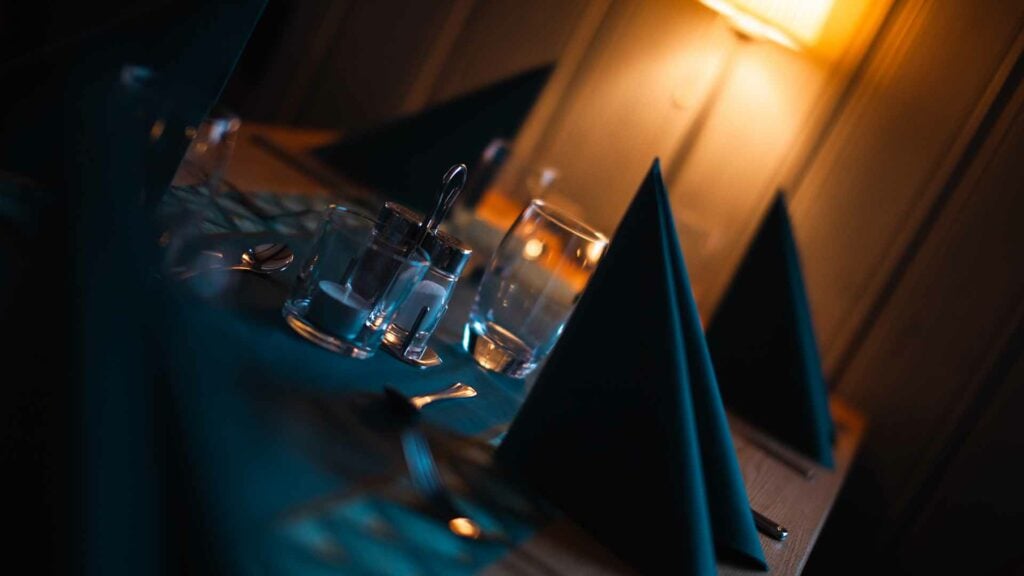 Romantisk bordsetting med tent lampe, glass og servise i dempet belysning.