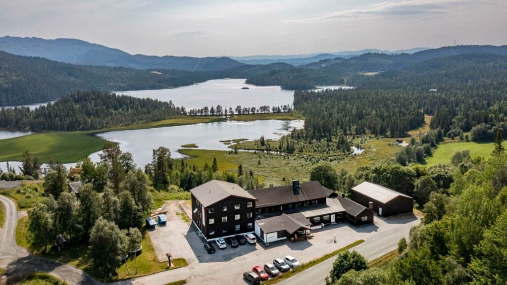 Flyfoto av norsk landskap med skog, innsjøer og bygninger, ideelt for naturopplevelser og rekreasjon.