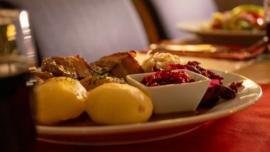 Tradisjonell norsk julemiddag med ribbe, poteter, rødkål og tyttebær i koselig belysning.