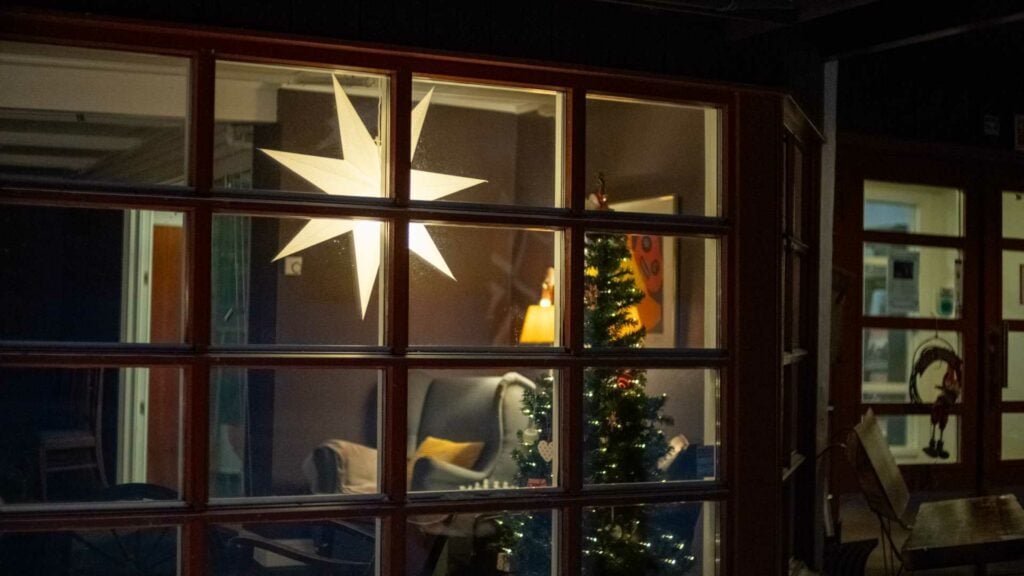 Utsikt gjennom vinduet til et julepyntet rom med en lysende julestjerne og et juletre innendørs.