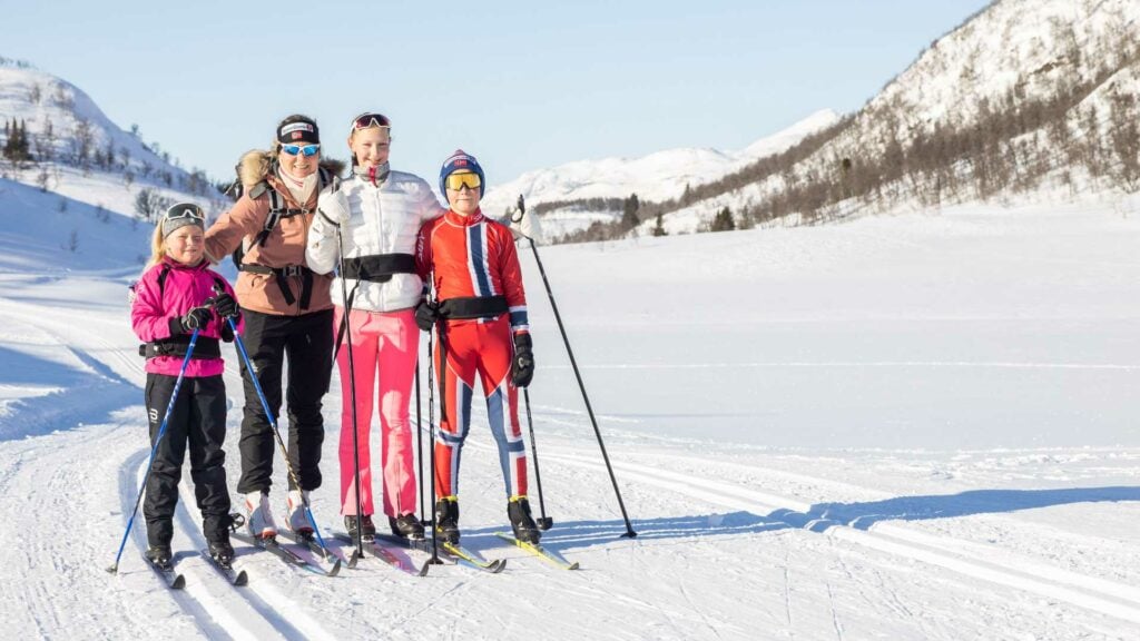Familie på skitur i snødekte fjell omgitt av klar blå himmel i Norge.