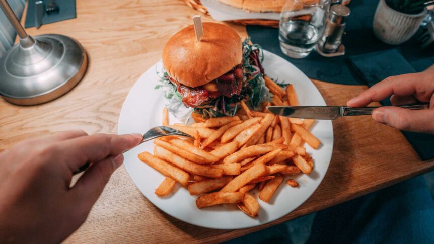 Burger med pomfritter på en hvit tallerken, klar til servering på et trefarget bord.