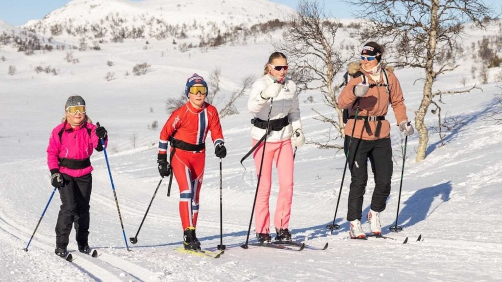 Familie på skitur i solfylt vinterlandskap, iført fargerike skikostymer.