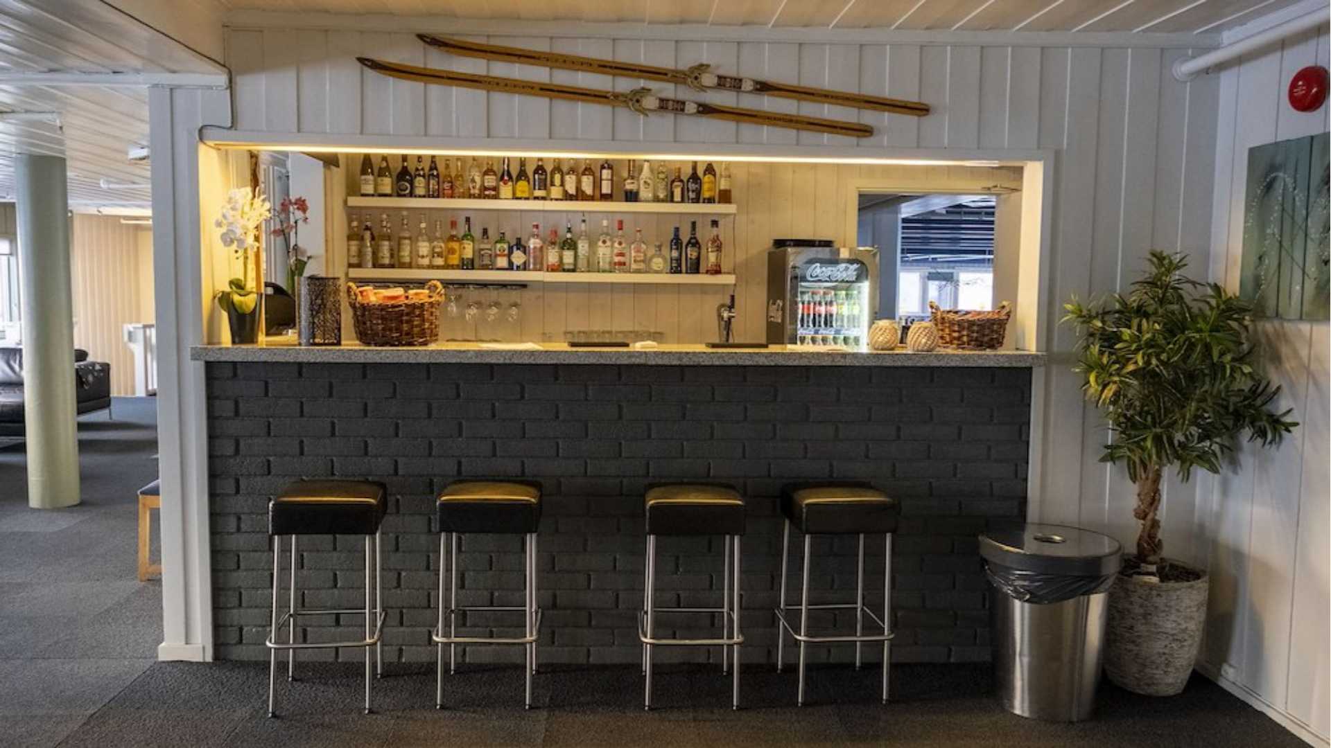 Koselig bar med svarte barkrakker, flasker på hyllen og ski på veggen.