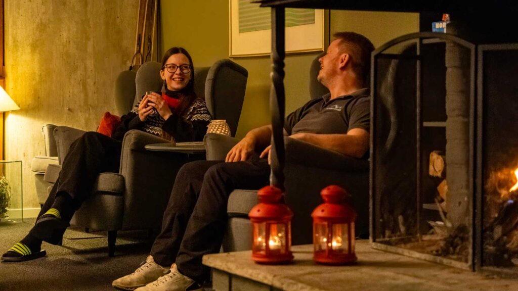 Personer slapper av i stue ved peisen, koselig atmosfære med røde lanterner.