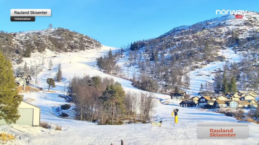 Snødekt landskap og skibakke ved Rauland Skisenter i solskinn, med fjell og hytter i bakgrunnen.