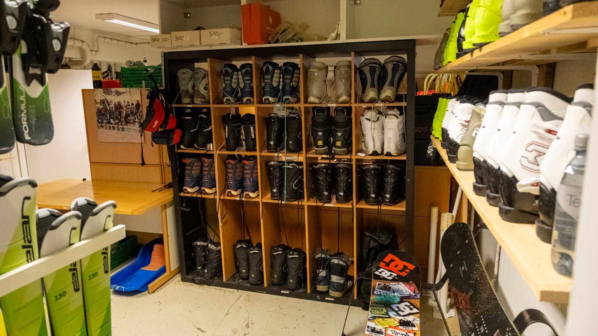 Skistøvler og snowboardstøvler i et skiskap, organisert på hyller i en vintersportsbutikk.