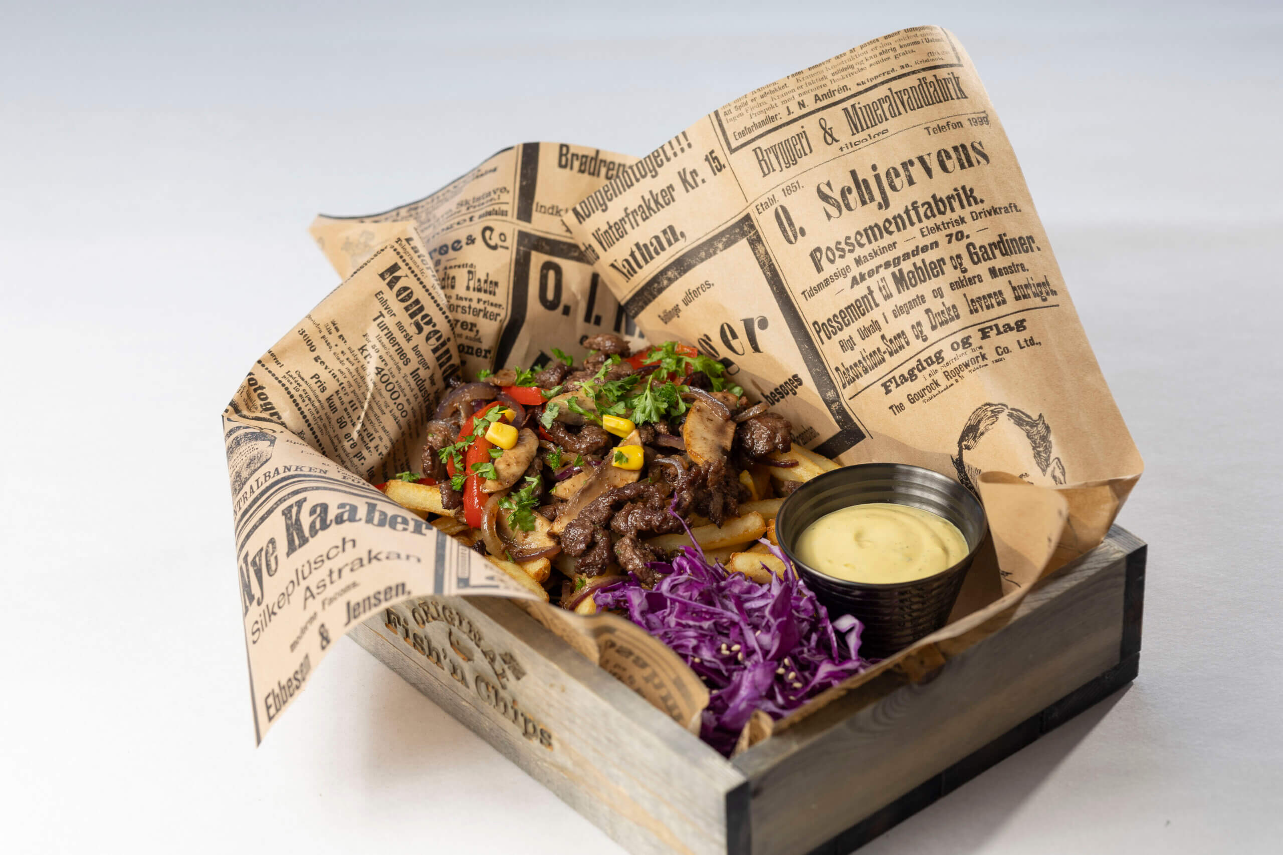 Gourmet biffretter i avispapir med grønnsaker, fries og dip, servert i en rustikk treboks.