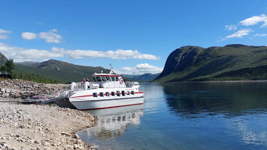 Båt ved naturskjønn kyst i Norge med fjell og klart vann under blå himmel.