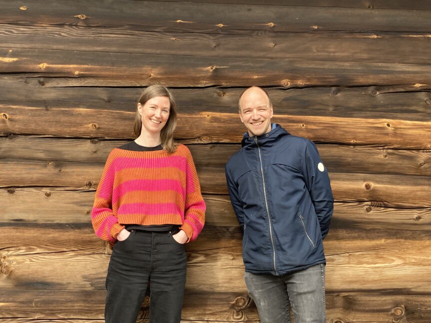 To mennesker smiler foran en vegg av treverk.