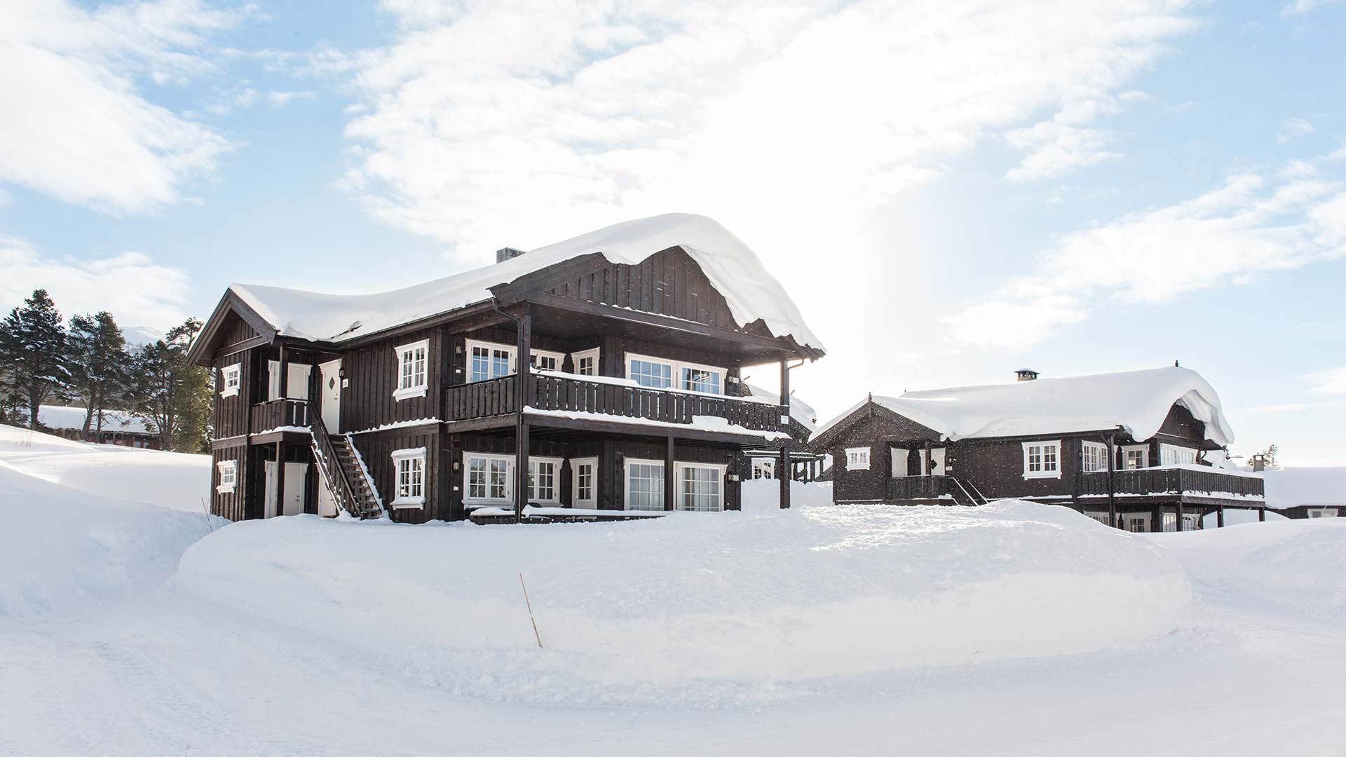 To tradisjonelle norske hytter med snødekte tak under en klar vinterhimmel.