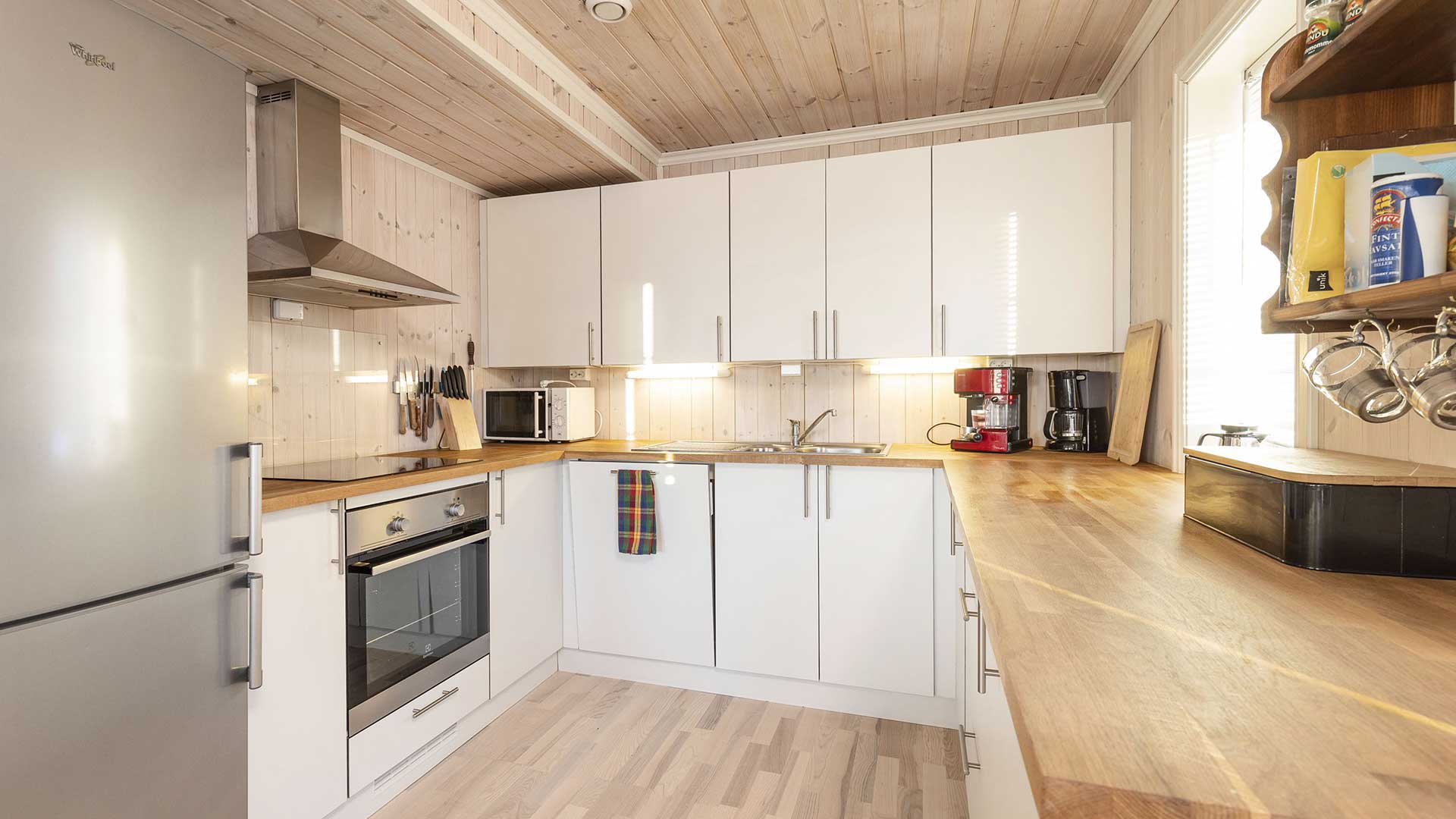 Moderne lyst kjøkken med hvite skap, trebenk og rustfritt stål-apparater. Koselig og funksjonell utforming.