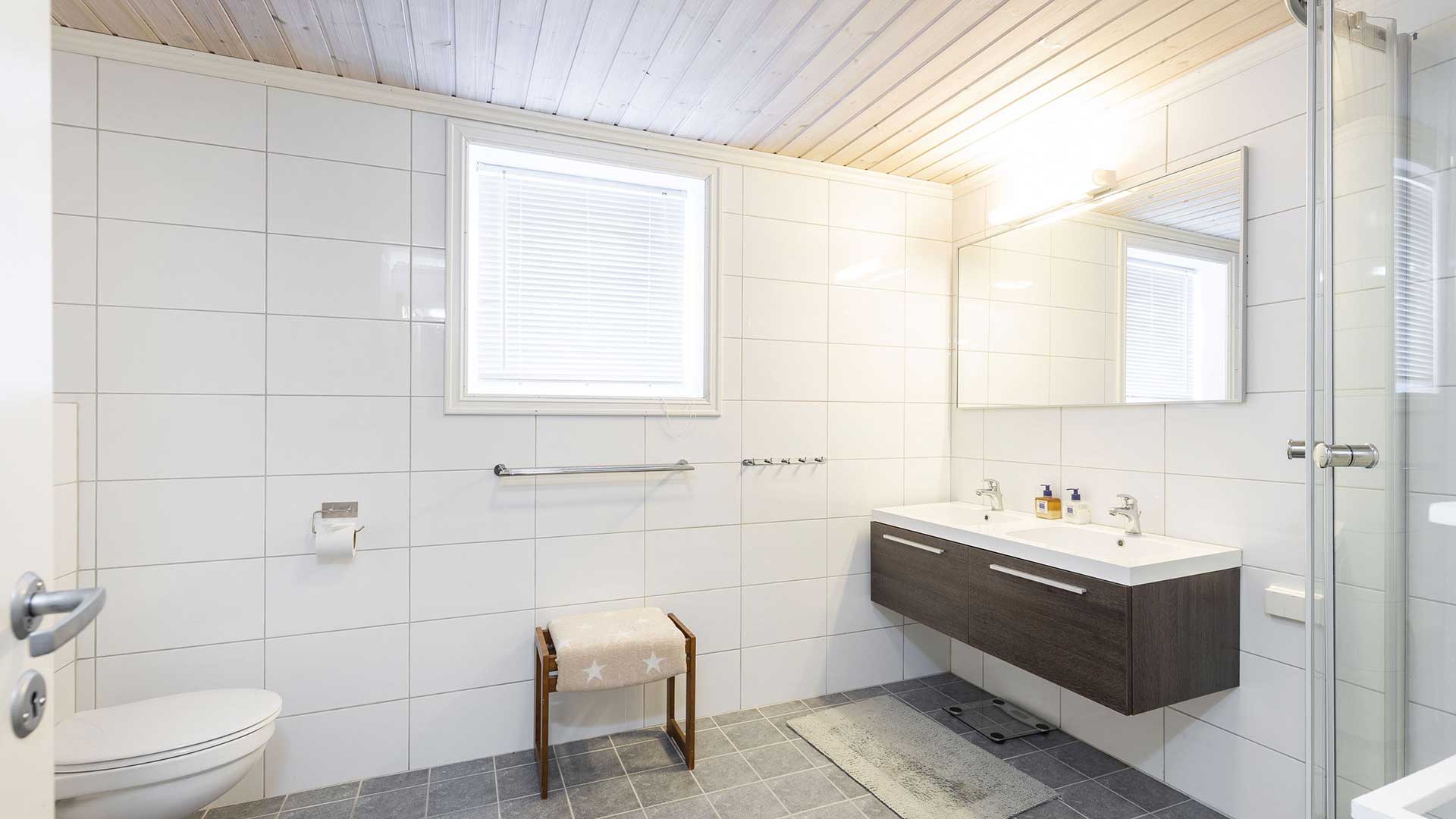 Lyst, moderne bad med dobbel vask, dusjkabinett og hvite fliser.