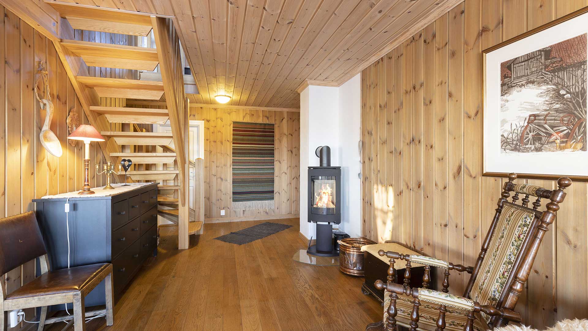 Treinteriør med trapp, peis og gyngestol. Koselig hytteatmosfære med varmeelementer og detaljer i tre.