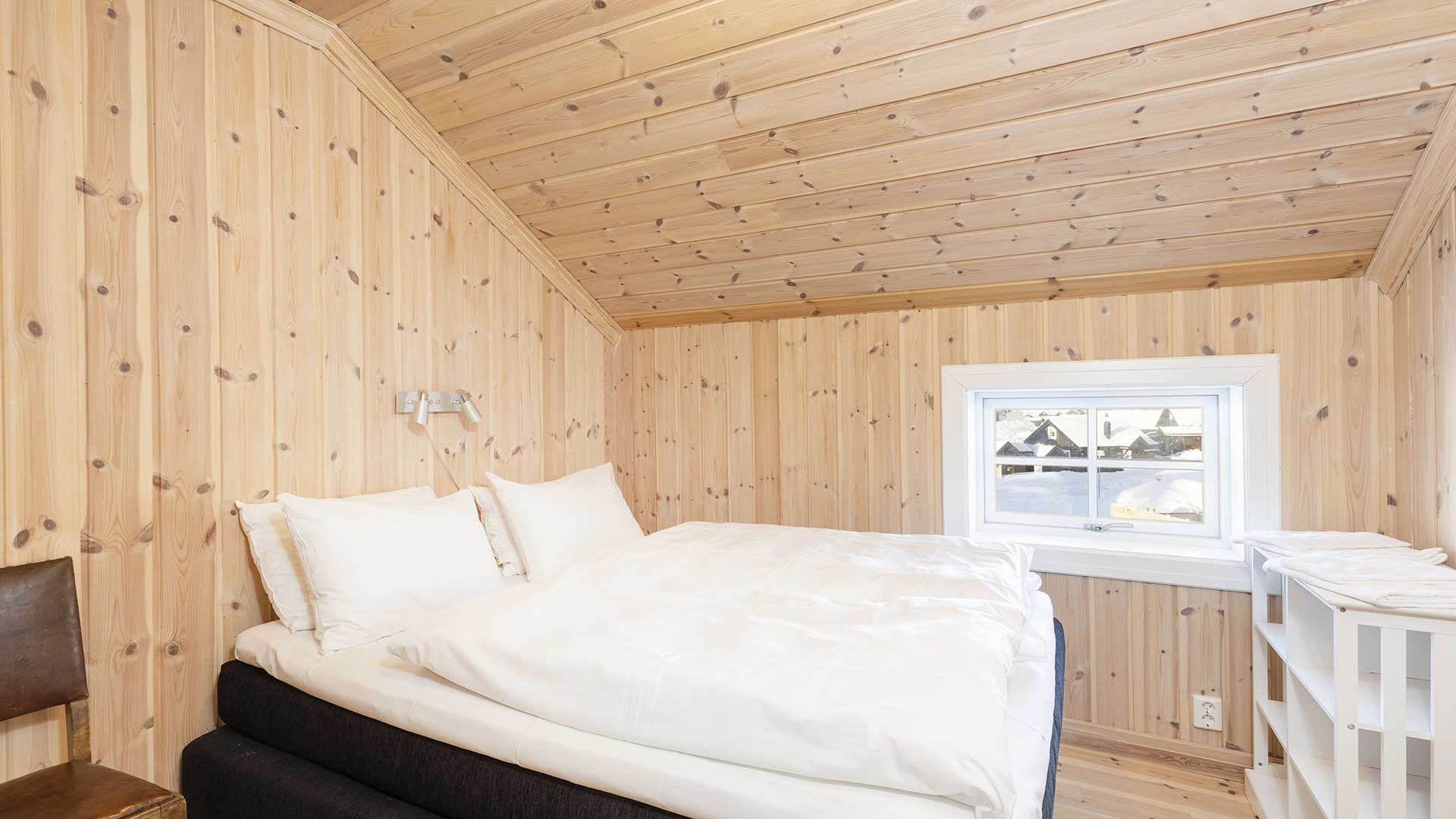 Koselig soverom med panelvegger og vindu med vinterutsikt, seng med hvitt sengetøy i en norsk fjellhytte.