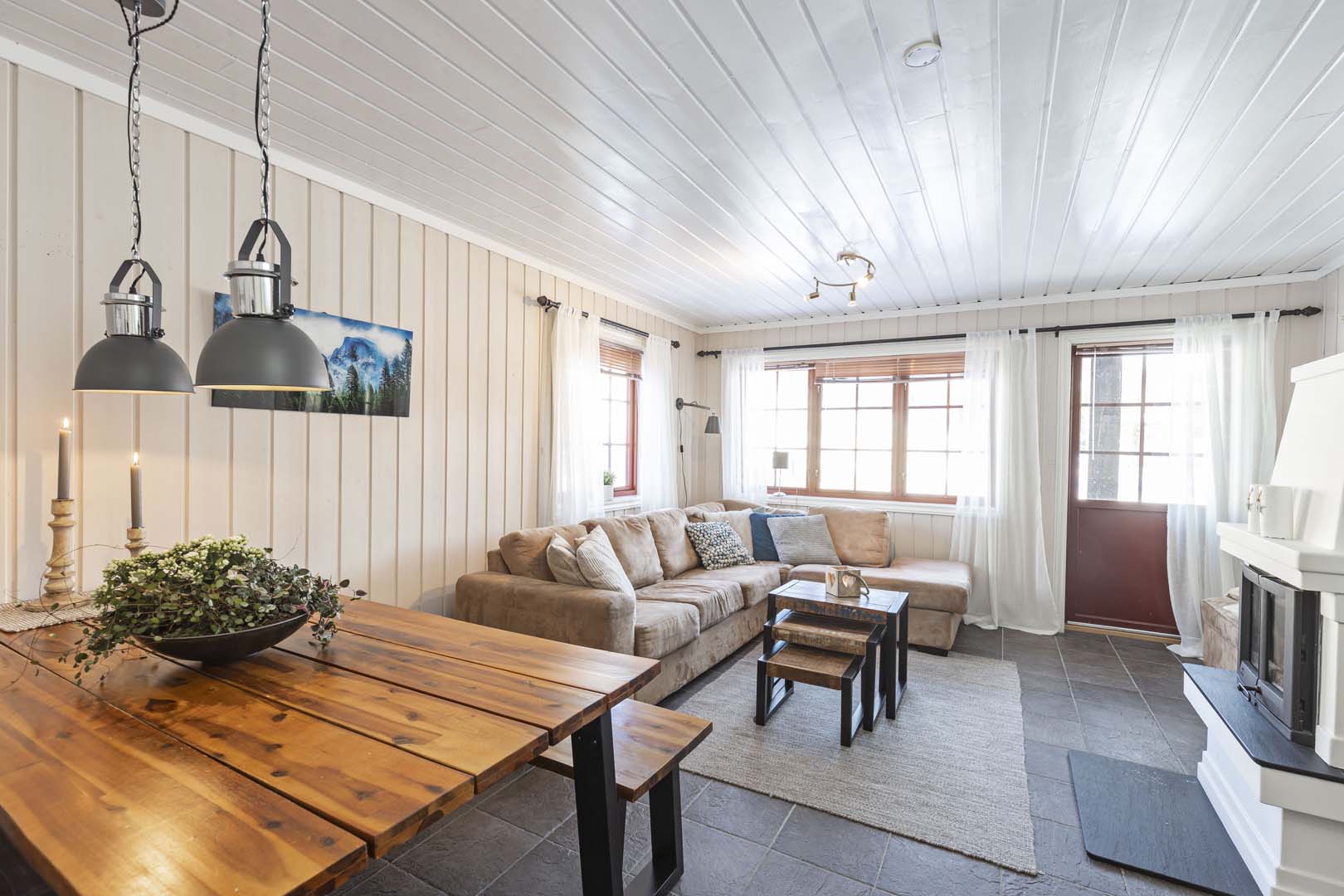 Koselig stue med peis, stor sofa, trebord, og store vinduer som slipper inn naturlig lys. Harmonisk interiørdesign.