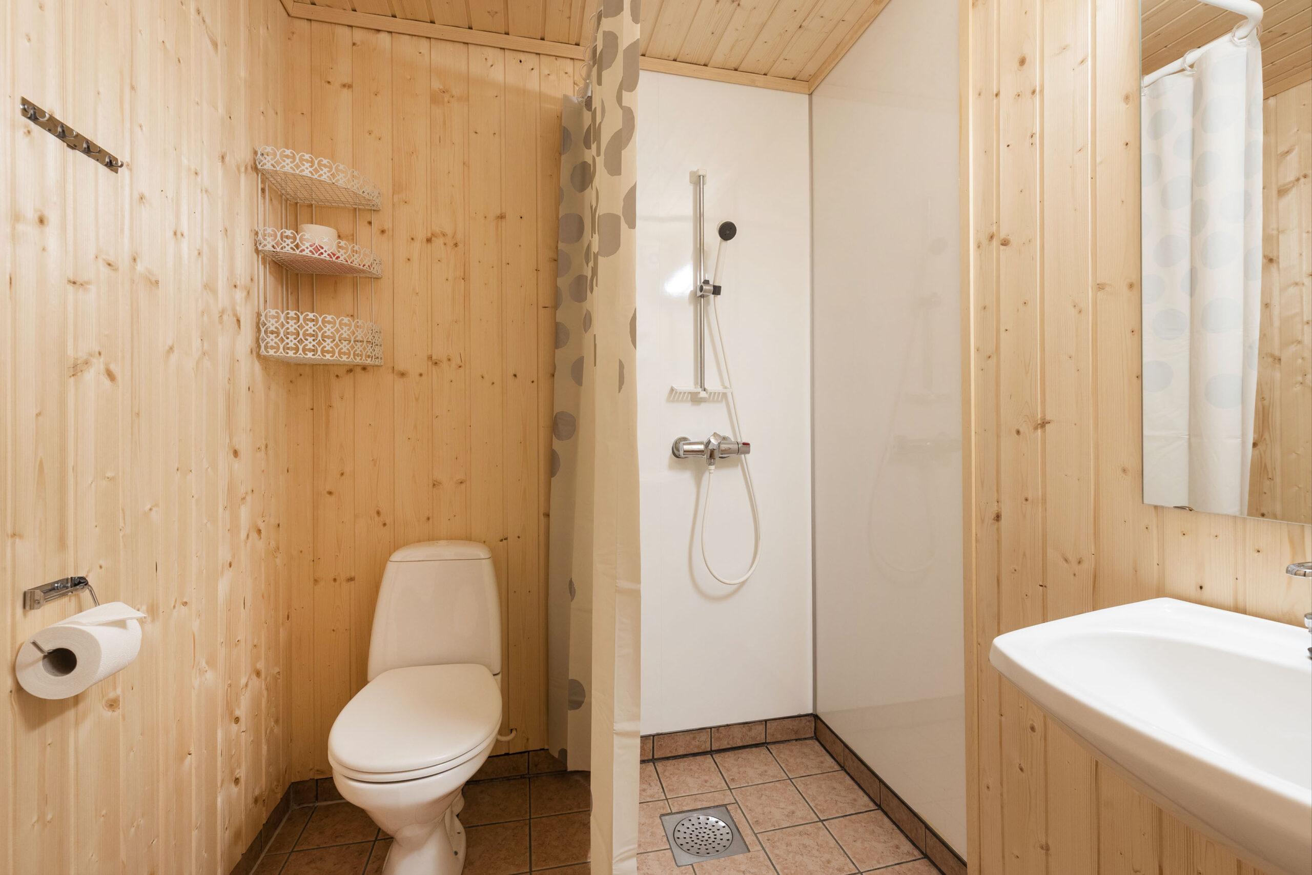 Lyst bad med treskjørte vegger, dusj, toalett og vaskeservant i cabin-stil.