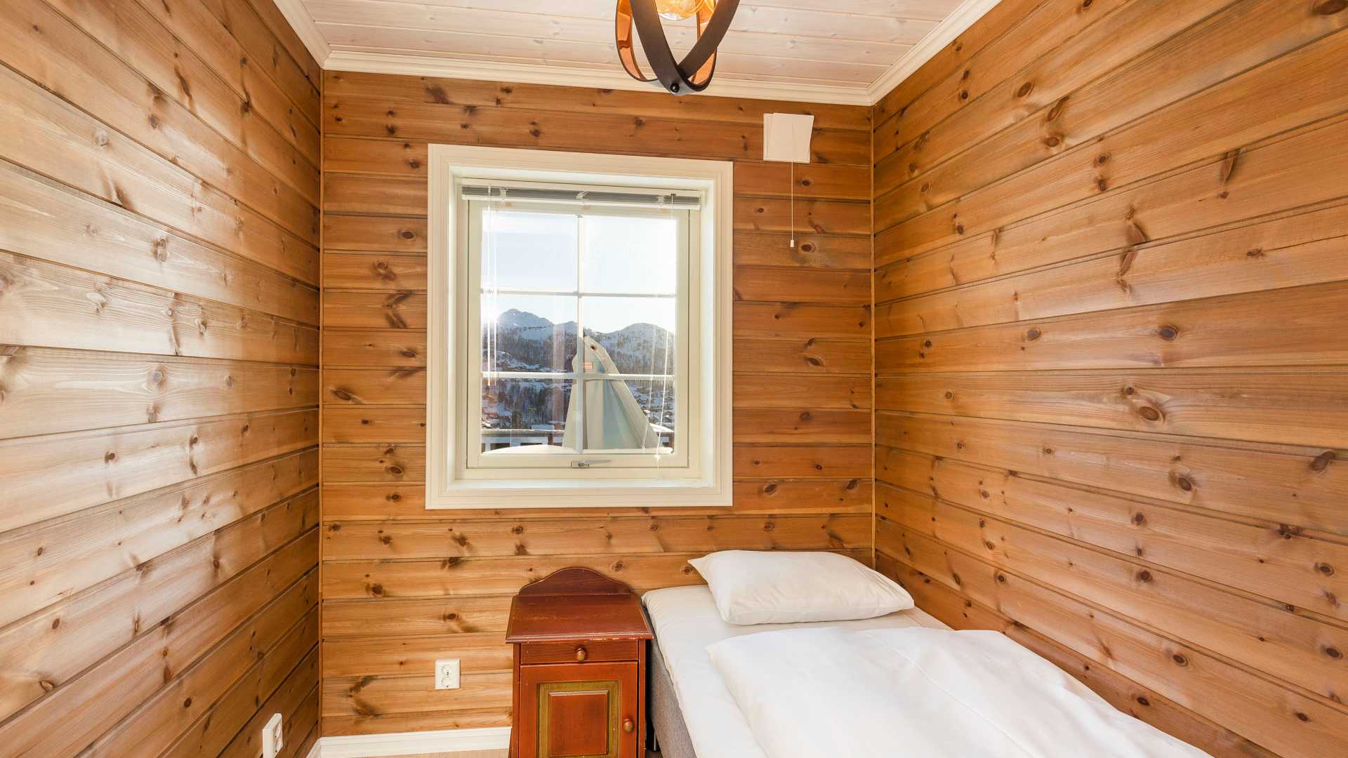 Liten tømmervegg soverom med enkeltseng og vindu, utsikt over fjell.