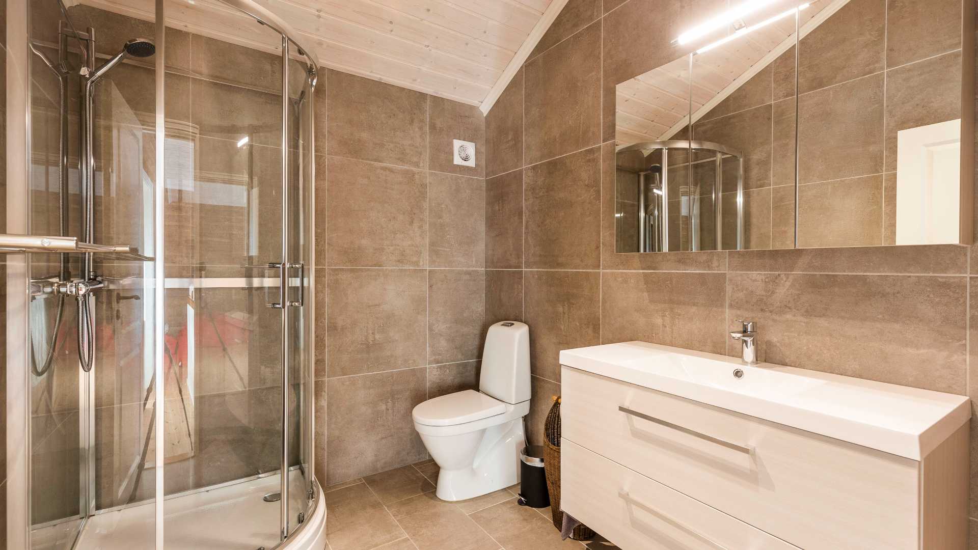 Moderne bad med dusjkabinett, toalett og speilskap. Lyse fliser og minimalistisk innredning.