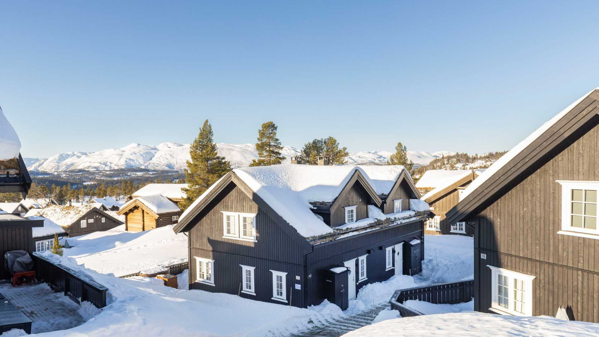 Skitilfytende hytter i snødekke fjellandskap under klar blå himmel i Norge.