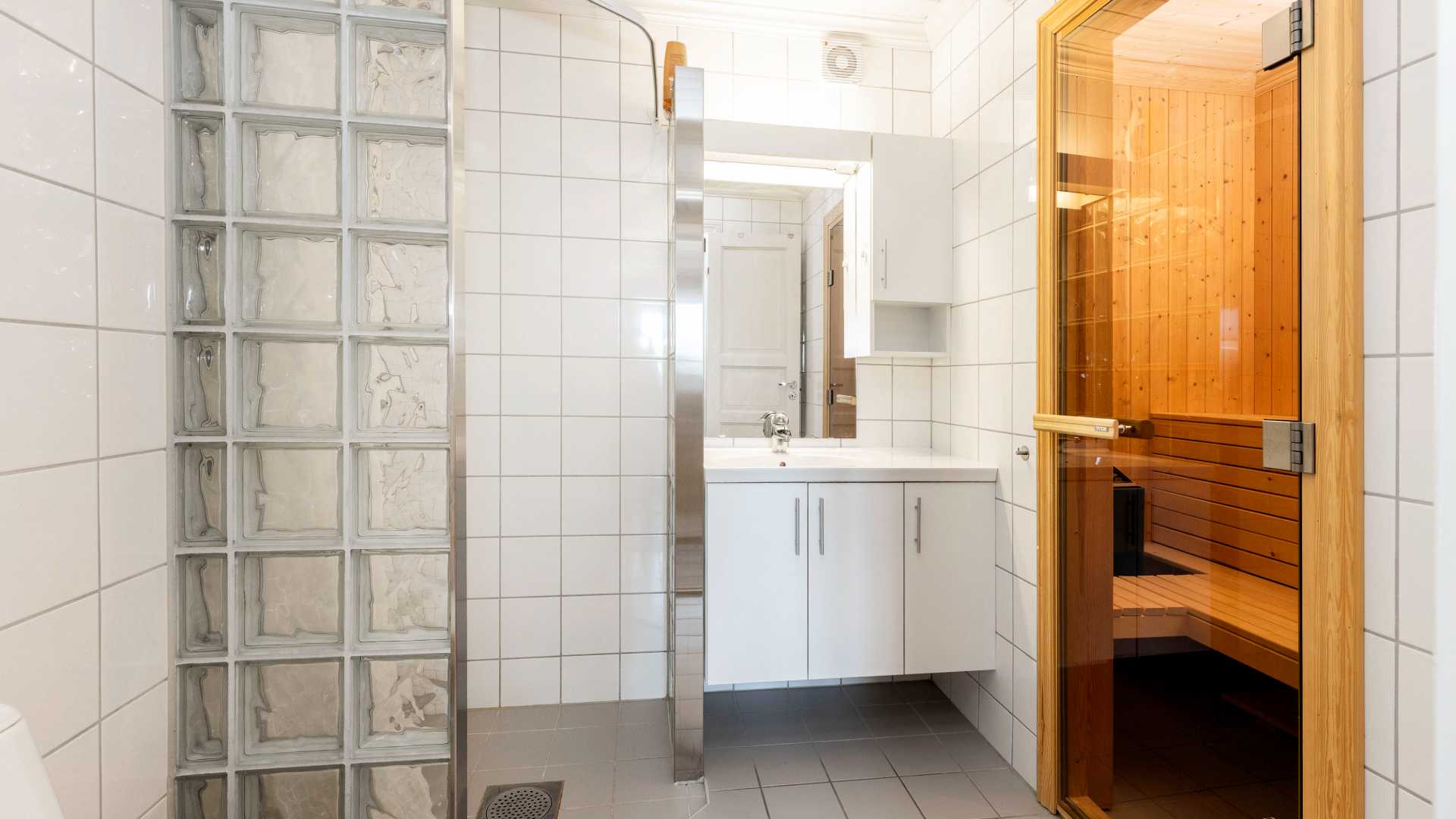 Moderne bad med fliser, vask og dør til trebadstue. Lys og romslig design for avslapning og velvære hjemme.