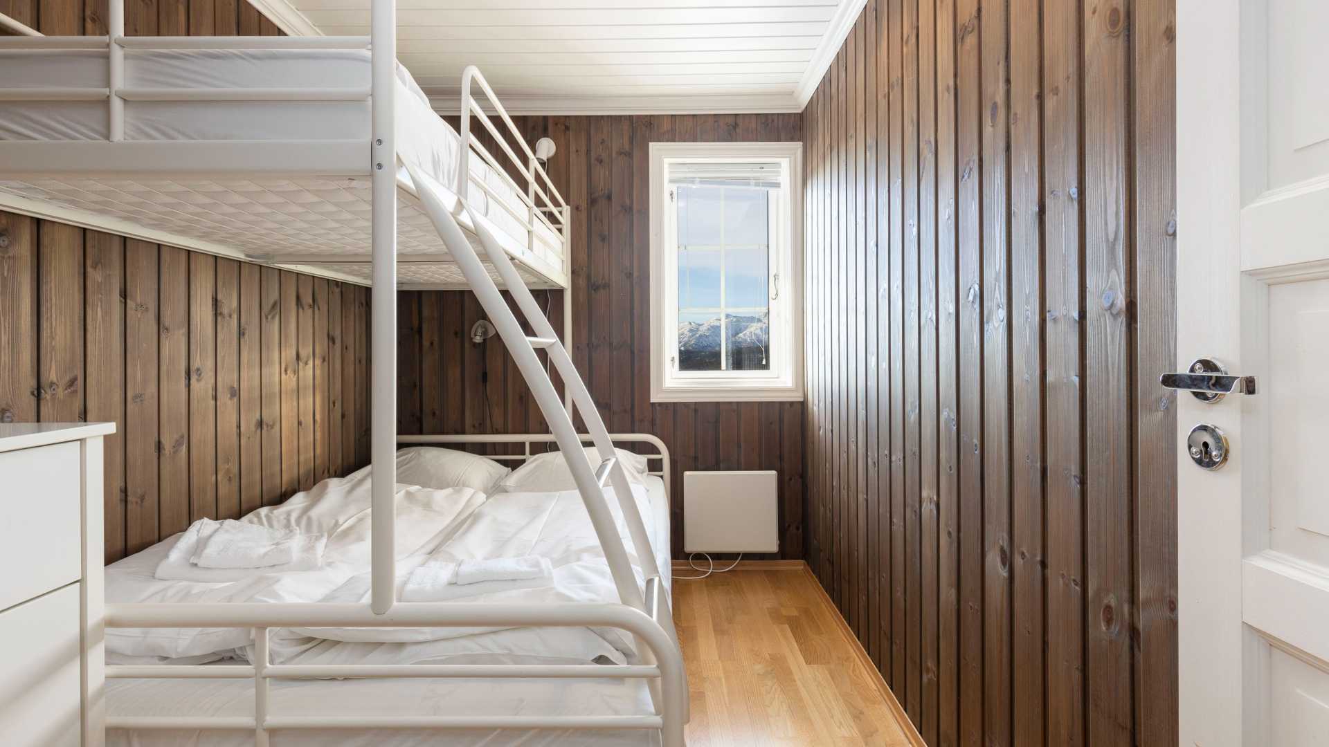 Lyst soverom med køyeseng, trevegger og vindu med utsikt over fjell. Koselig og minimalistisk interiørdesign.