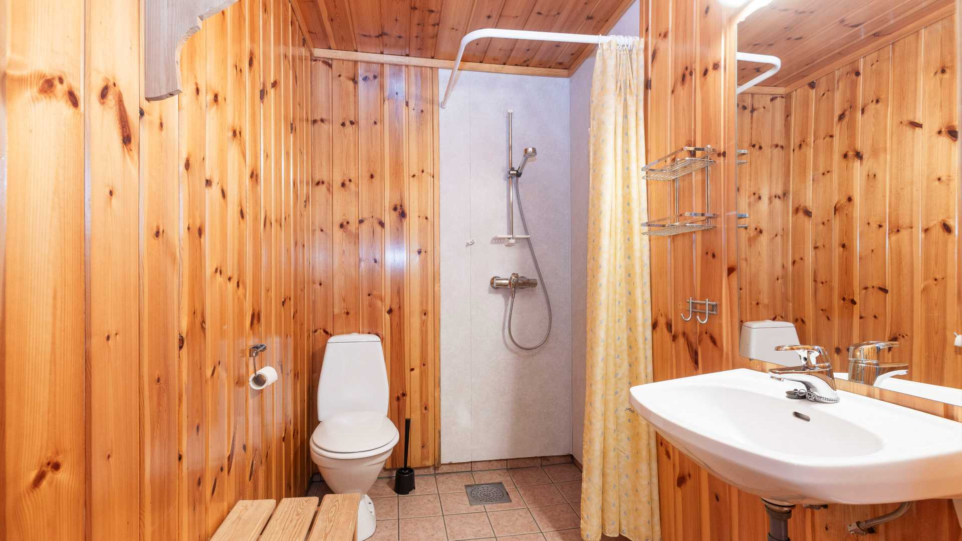 Bad med furupanelvegger, dusj, toalett og servant. Rustikk og koselig innredning.