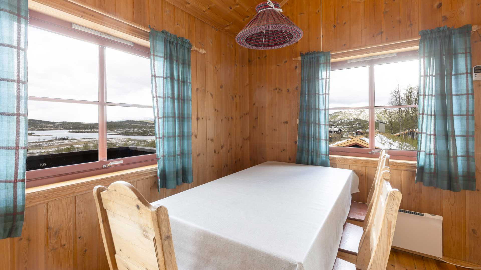 Koselig spisestue i hytte med utsikt over fjellandskap gjennom store vinduer.