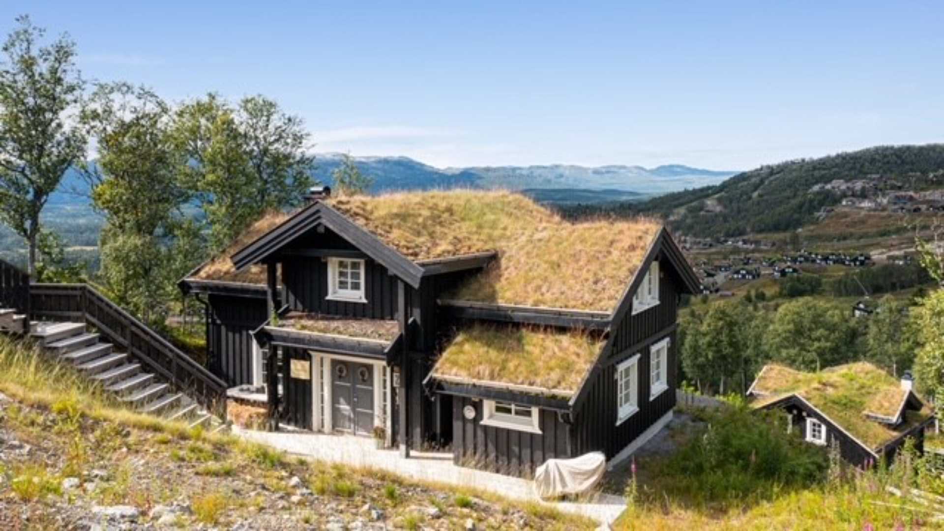 Tradisjonell norsk hytte med torvtak, omgitt av vakker utsikt over dalen og fjellene i bakgrunnen.