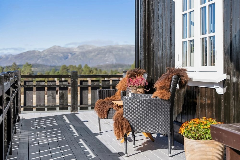 Solrik terrasse med fjellutsikt, to kurvstoler med saueskinn, blomsterdekorasjon, idyllisk norsk natur.