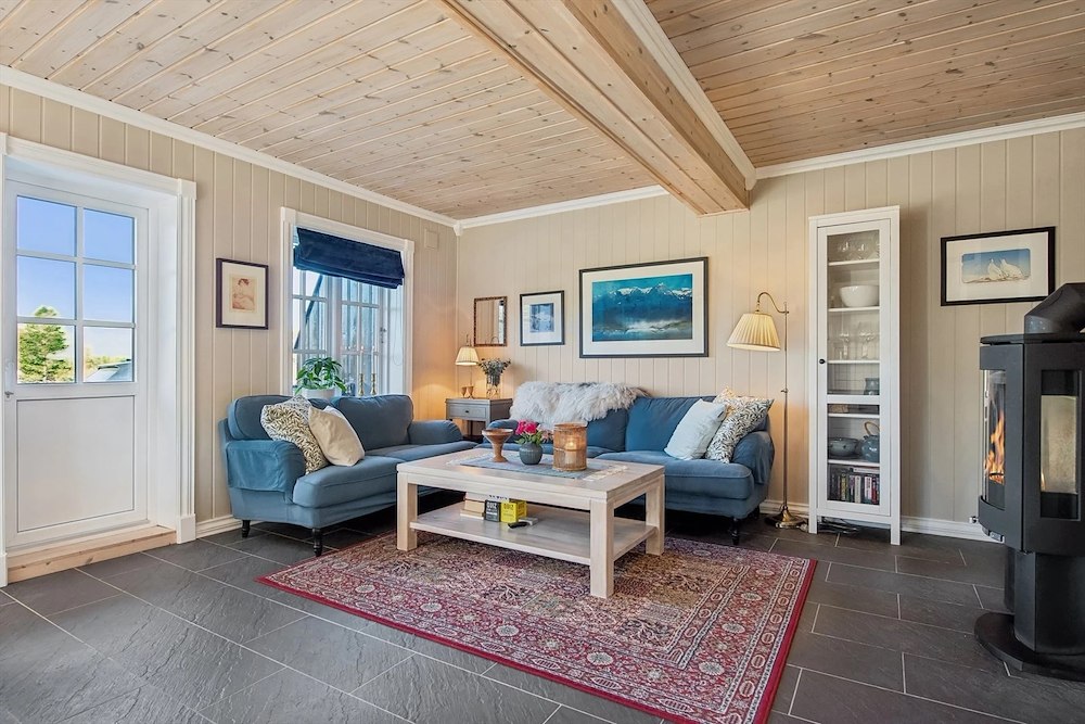 Lys og koselig stue med blå sofa, peis, og naturlige trepaneler. Elegant skandinavisk design.
