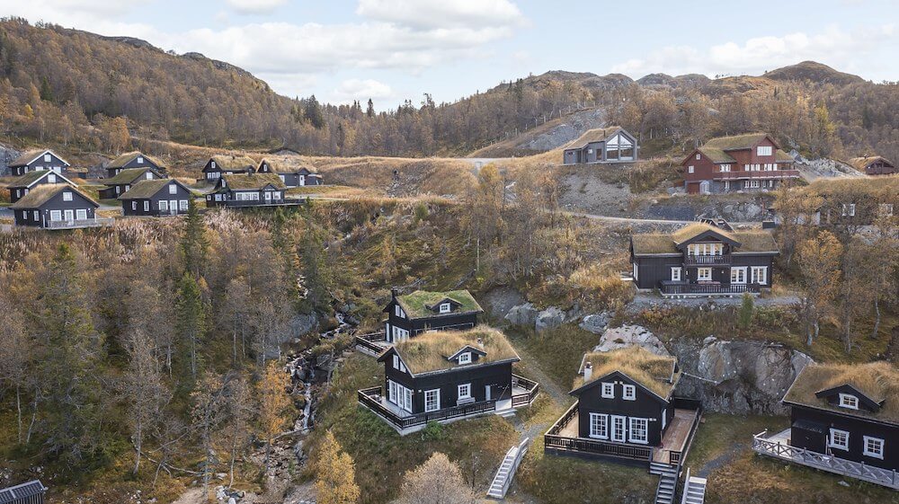 Hyggelige norsk fjellhytter med torvtak i naturskjønn fjellandskap omringet av høsttrær.