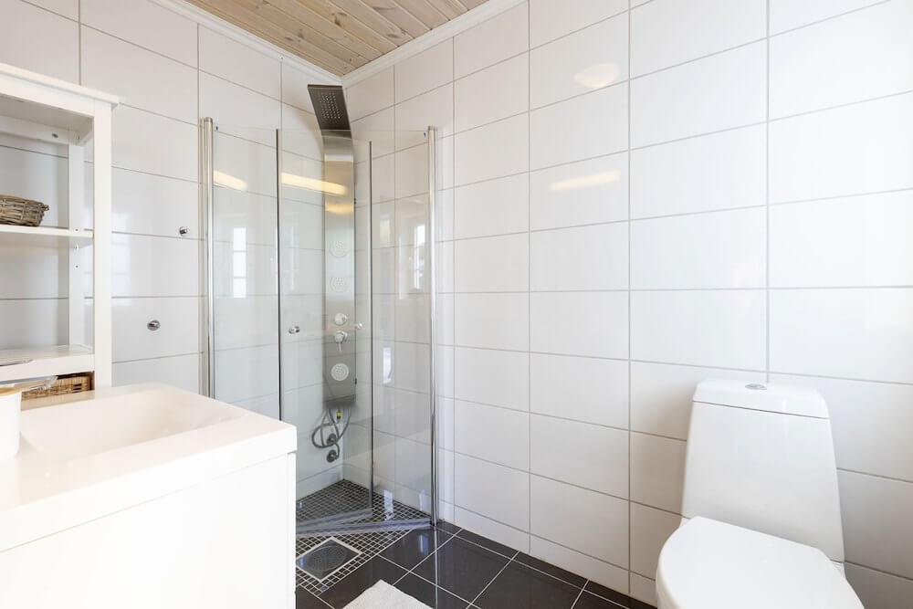 Lyst og moderne bad med dusjkabinett, toalett og vask i hvite fliser.