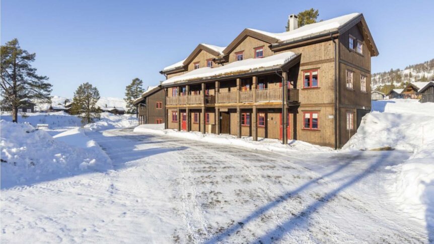Tømmerhus i snødekt vinterlandskap med blå himmel, ideelt for hytteferie i Norge.