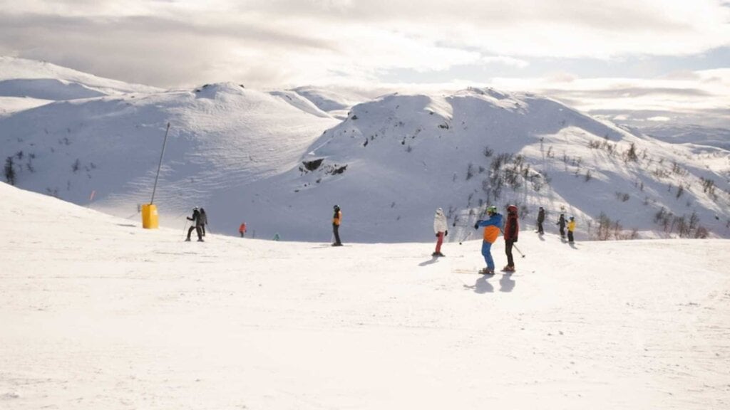 Folk som står på ski i solfylt, snødekket fjellandskap i Norge, med klare himmel og naturskjønne bakgrunner.