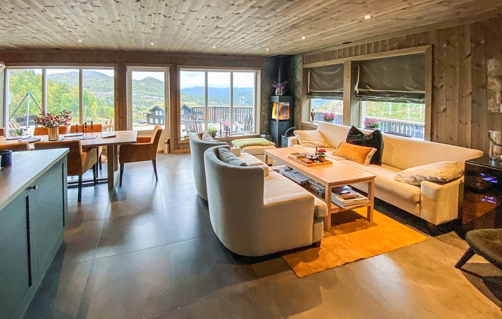 Lyst og romslig stue med moderne interiør, store vinduer og utsikt over fjell og dal.