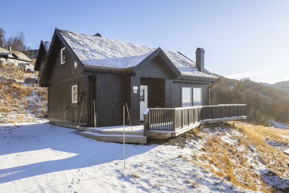 Svart hytte med snødekt tak i naturskjønt fjellandskap om vinteren.