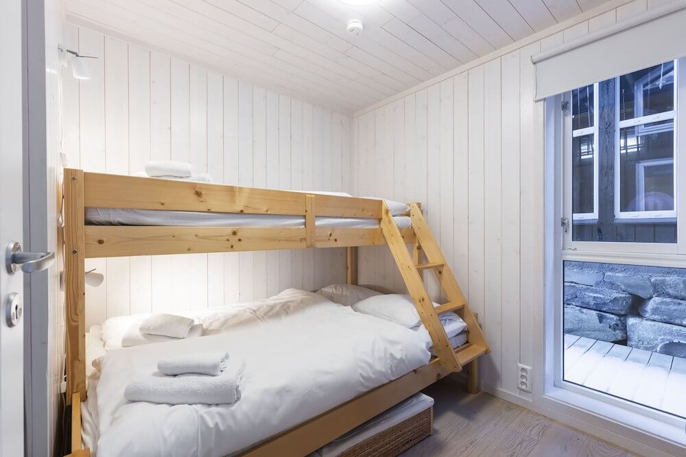 Toetasjeseng i lyst skandinavisk soverom med myke hvite sengetøy og vindu mot uteområde. Koselig innredning.