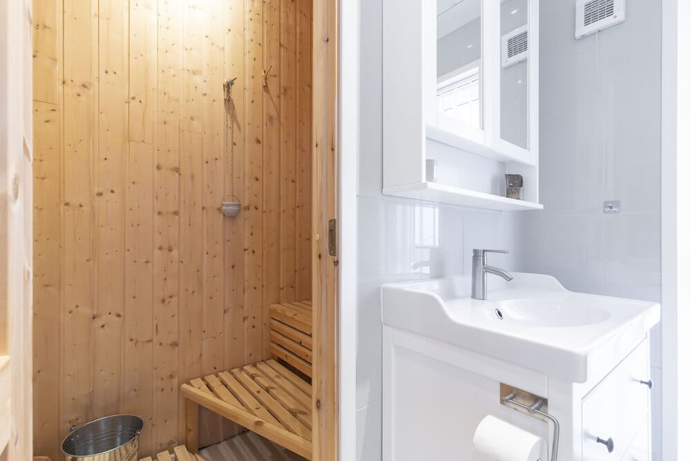Moderne bad med hvit vask og vedfyrt badstue i treverk. Minimalistisk interiørdesign.