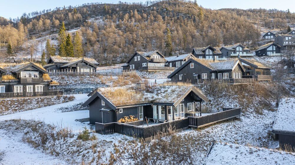 Snødekte hytter i norsk fjellandskap, trær i bakgrunnen, klar vinterdag.