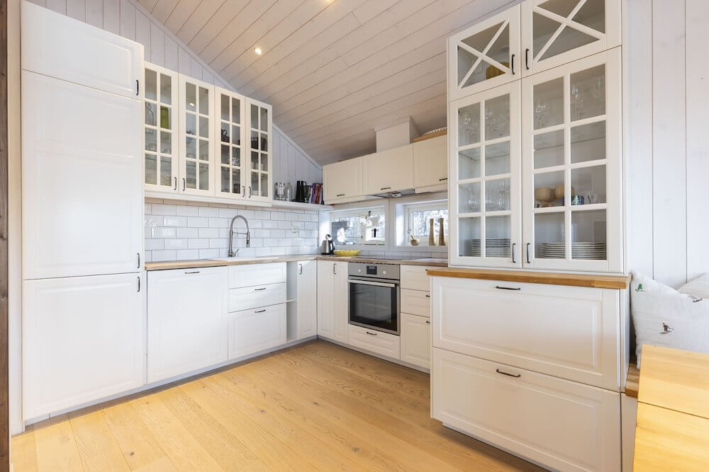 Lyst, moderne kjøkken med hvite skap, trebenk og innebygd stekeovn. Lyst tregulv og flislagt vegg.