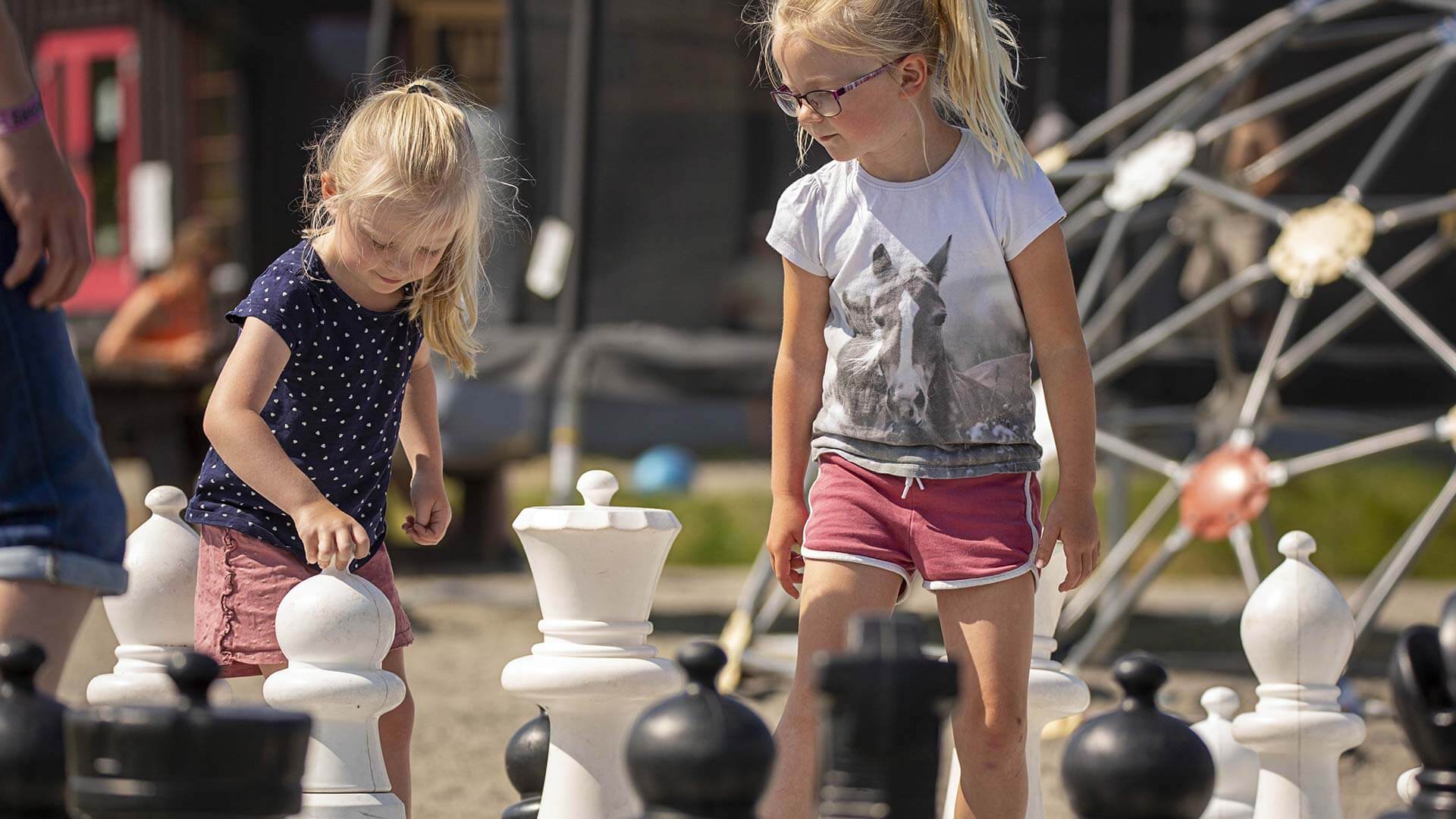 To barn spiller sjakk med store brikker utendørs på en solrik dag.
