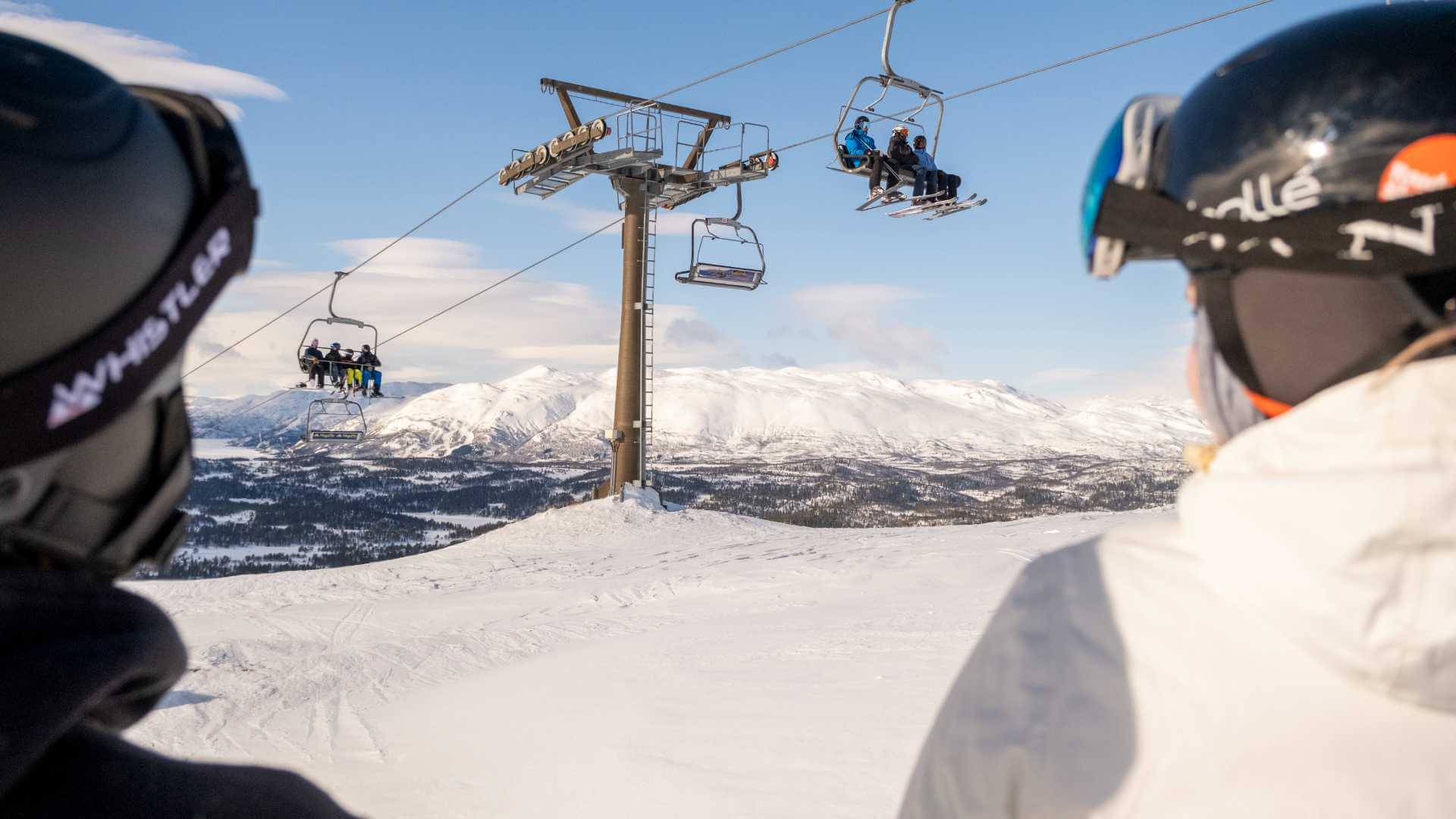 Skiturister i heisen med snødekte fjell i bakgrunnen. Klar blå himmel. Vintersport i Norge.