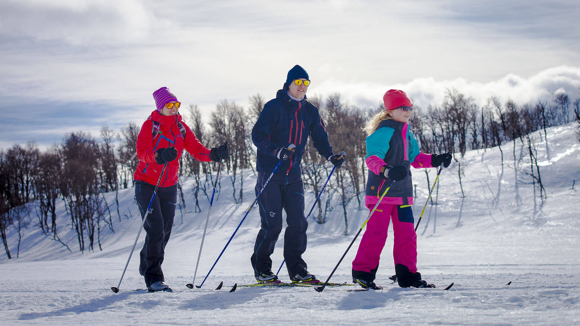 Tre personer går på langrenn i snødekte fjell med klar himmel.