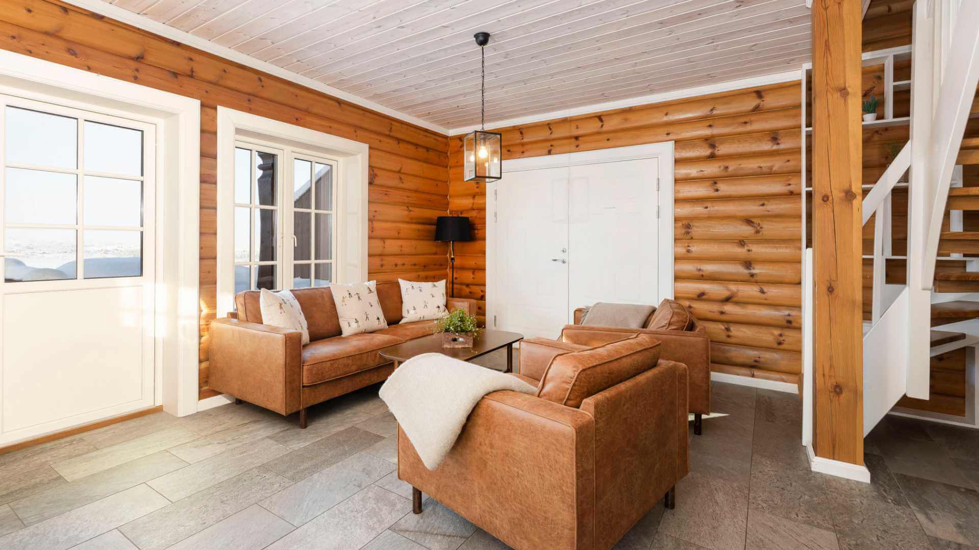 Koselig stue med tremøbler og naturlig lys, skinnsofaer og trebjelker. Perfekt for avslapning og hygge.