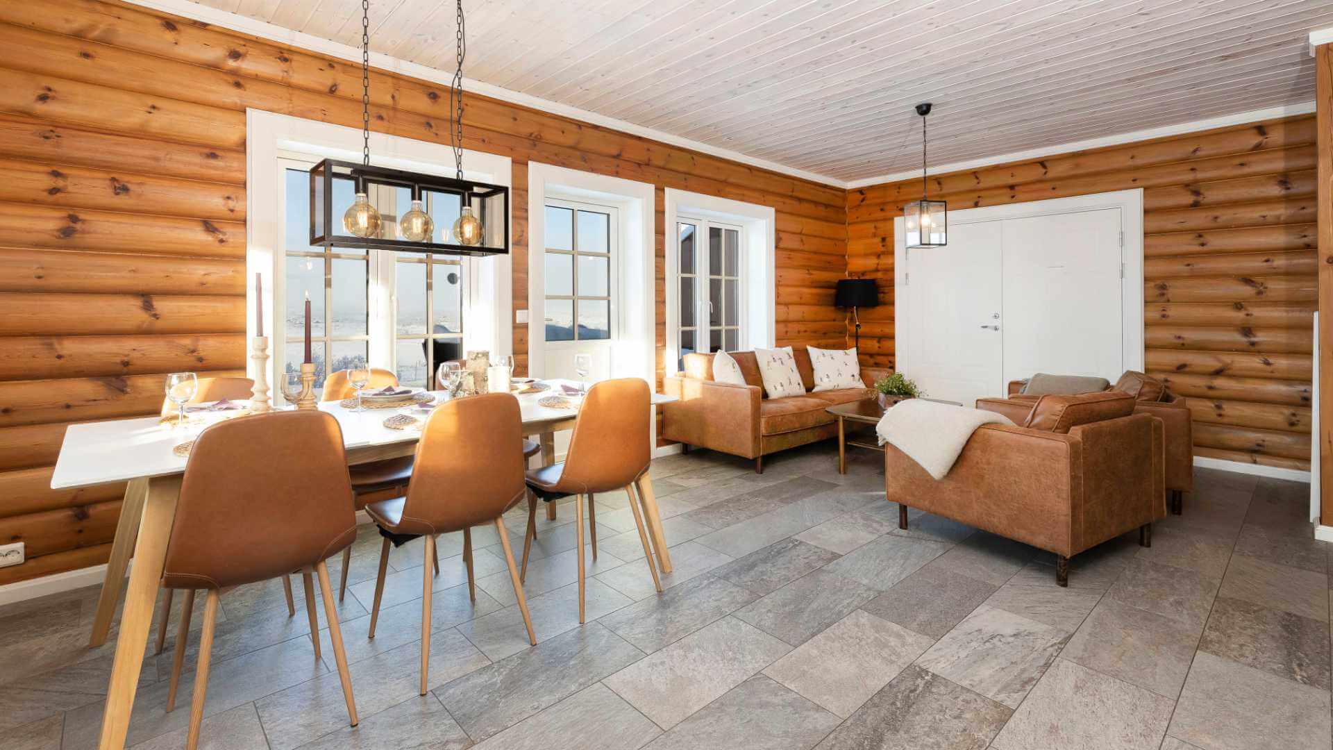 Koselig stue med tømmervegger, spisebord, og sofagruppe i brun lær for en rustikk atmosfære.