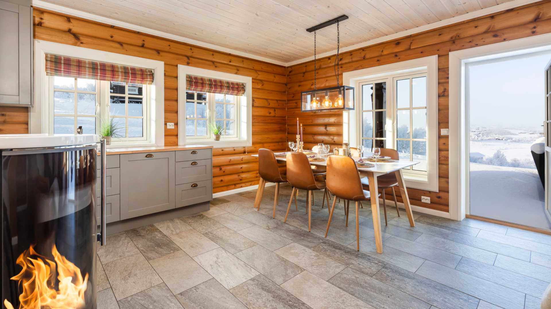 Moderne hytteinteriør med spisebord, peis og vinterutsikt gjennom store vinduer. Koselig og stilfullt design.