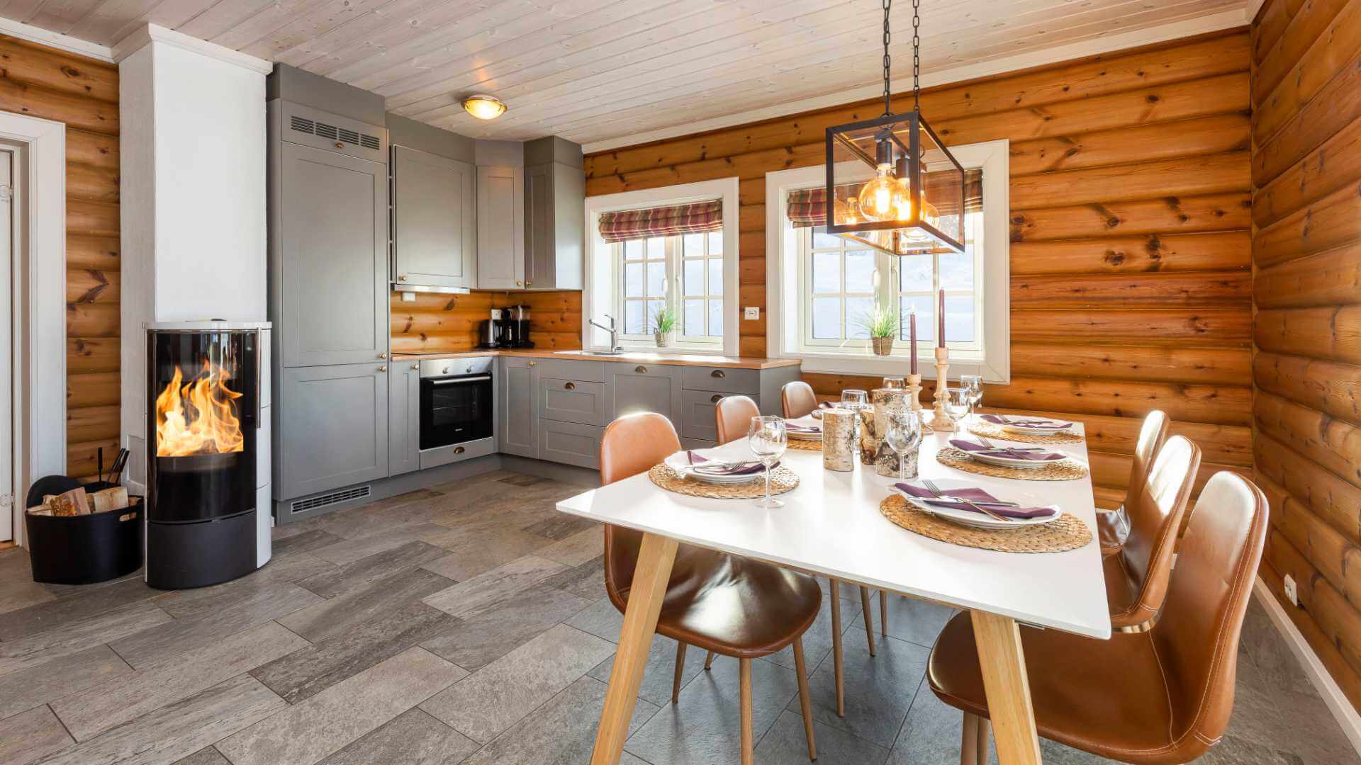 Koselig kjøkken med trepanel, peisovn, moderne innredning og spiseplass dekket til fire personer.