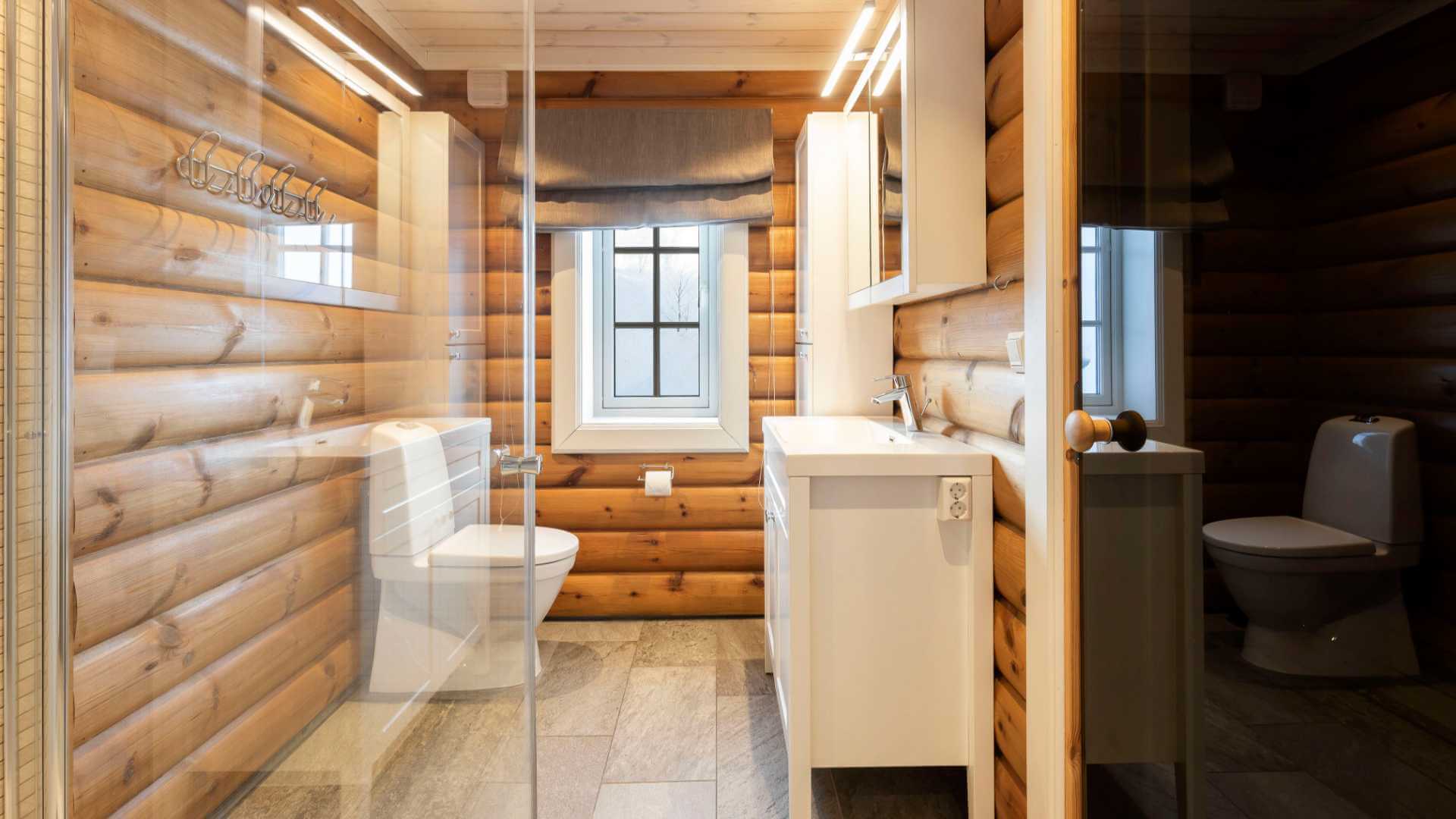 Lyst bad med tømmervegger, stor dusj, hvit servant, vindu og moderne innredning.