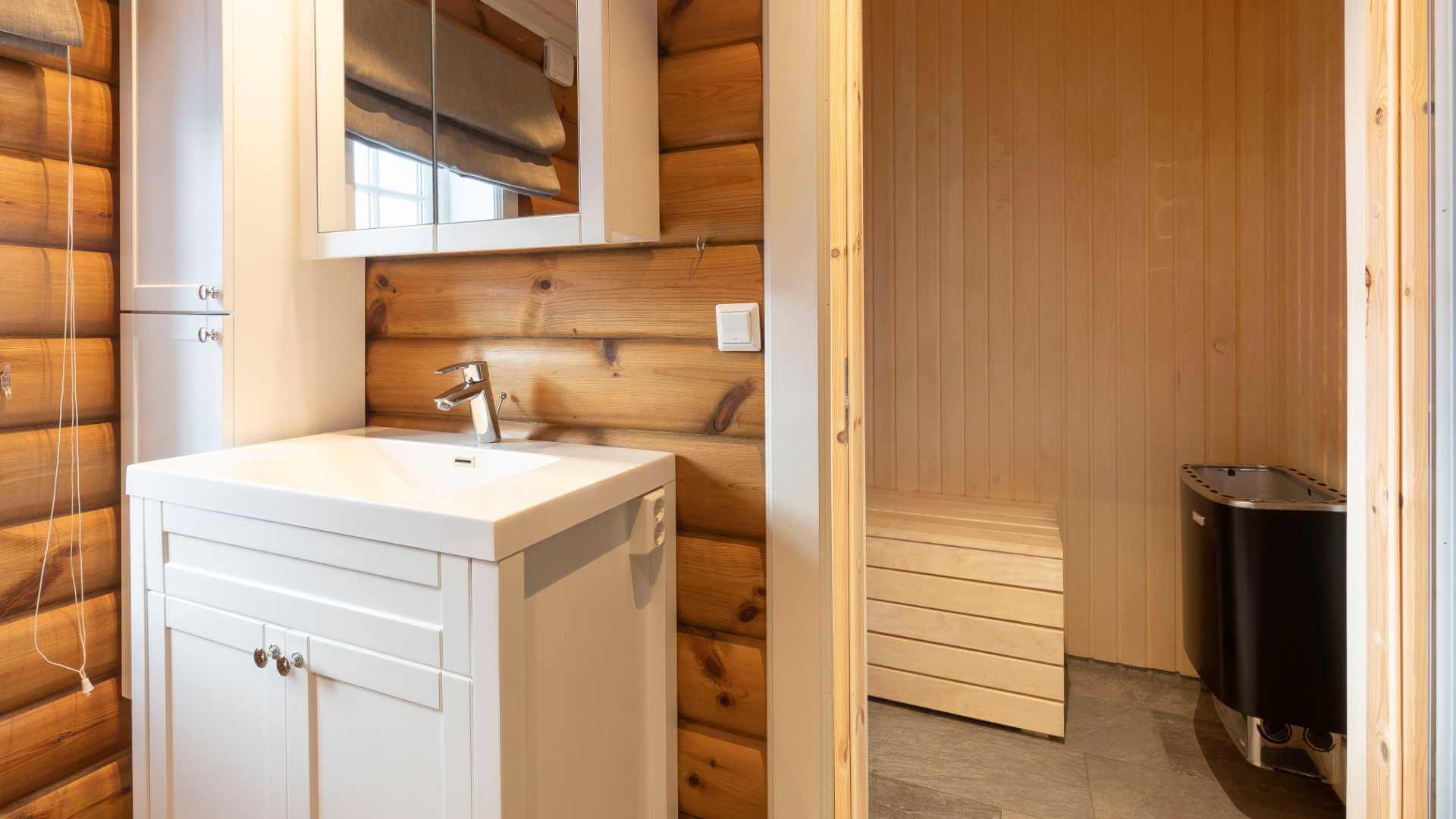 Moderne bad med servant i trehus, ved siden av inngang til badstue i naturmaterialer.